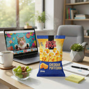Laptop on a desk with a bag of Uncle Ray's Cheddar Puffcorn, coffee, and snacks.
