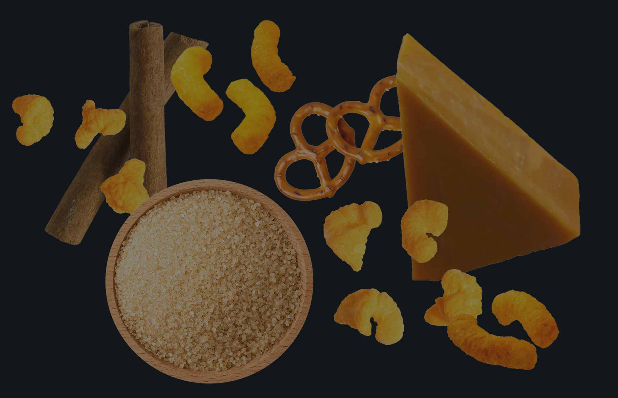 Spices and seasonings including a block of cheese, cinnamon sticks, and dried fruits on a black background.